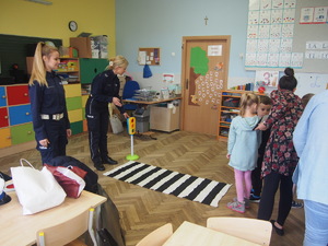 w sali przedszkola policjantki uczą dzieci przechodzić przez jezdnię na prowizorycznie przygotowanym przejściu dla pieszych z sygnalizacją świetlną