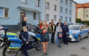 Dzieci i młodzież z OSP Oświęcim w oświęcimskiej komendzie wspólne zdjęcie dzieci, policjanci na tle radiowozu i motocykla