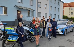 Dzieci i młodzież z OSP Oświęcim w oświęcimskiej komendzie wspólne zdjęcie dzieci, policjanci na tle radiowozu i motocykla