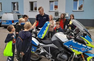 Dzieci i młodzież z OSP Oświęcim w oświęcimskiej komendzie  policjant wrd przy motocyklu dzieci stoją obok