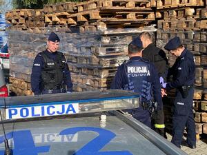 policjant zakładający kajdanki zatrzymanemu podpalaczowi, obok inni policjanci