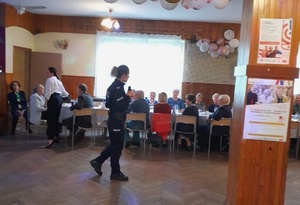 policjantka prowadzi spotkanie dla grupy seniorów w sali budynku Rodzinnych Ogrodów Działkowych