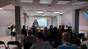 dwoje policjantów prowadzących prelekcje, za nimi prezentacja, przed nimi siedzący uczestnicy spotkania, widoczni tyłem do zdjęcia