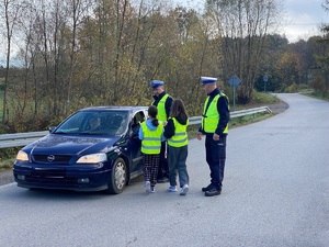 policjanci stojący przy niebieskim samochodzie i dwie dziewczynki wręczające odblaski kierowcy