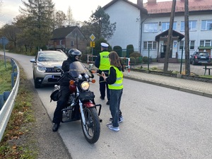 policjant i dziewczynka wręczająca odblaski motocykliście oraz kierowcy samochodu