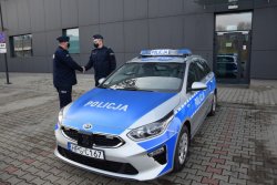 Radiowóz policyjny oznakowany, przy nim stojący Komendant Powiatowy gratuluje Komendantowi Komisariatu w Zielonkach otrzymanego radiowozu