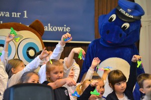 Uczniowie szkoły prezentują otrzymane zawieszki odblaskowe. Obok maskotka policji - Smok Wawelek