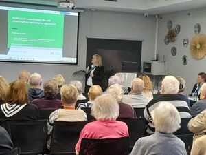 Dzień seniora pracowniczka ZUS podczas prezentacji seniorzy siedzą na krzesłach