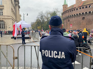 umundurowany policjant stojący tyłem do zdjęcia obserwujący osoby znajdujące się na jednej z ulic Krakowa