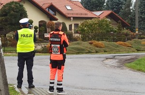 Akcja Żyj i ratuj życie w Jawiszowicach policjant i nauczyciel ratownictwa stoją przy drodze. Policjant mierzy prędkość
