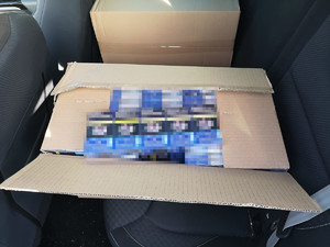 otwarte pudło kartonowe z zawartością paczek nielegalnych papierosów, leżące na tylnym siedzeniu pojazdu