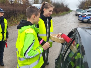 dwoje uczniów w kamizelkach odblaskowych częstuje kierowcę lizakiem