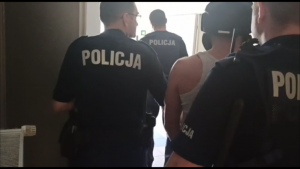 zatrzymany w hełmie zabezpieczającym zakuty w kajdanki prowadzony przez trzech policjantów