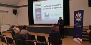 Na sali siedza osoby i funkcjonarisze Policji, którzy słuchają wypowiedzi przedstawiciela lokalnego samorządu