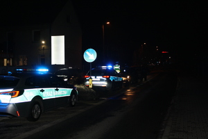 stojący pojazd Straży Granicznej, przed nim radiowóz policyjny i przed nim z koeli stojący policjant zatrzymujący pojazdy.