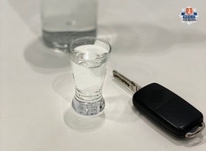 napełniony kieliszek za którym stoi pełna butelka a obok kluczyki od samochodu na białym stole