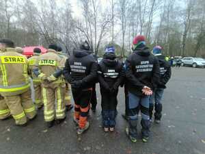 Grupa mężczyzn z napisami na plecach w czarnych kurtkach- "grupa ratownictwa medycznego"