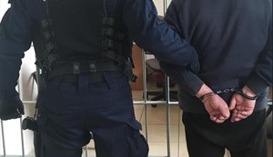 KPP Oświęcim. Policjant z zatrzymanym stoją przed kratami