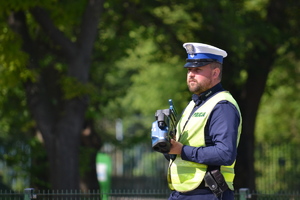 Policjant ruchu drogowego trzyma w ręce miernik prędkości, nadzoruje ruch na drodze