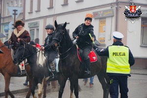 policjant ruchu drogowego w białaje czapce wręcza odblaski osobą jadącym na koniach w czasie pochodu