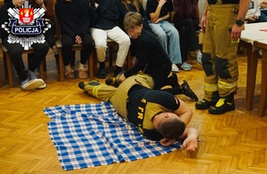 chłopiec na strażaku ćwiczy ułożenia poszkodowanego w pozycji bezpiecznej