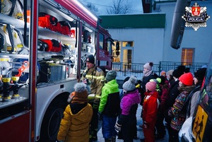 dzieci stojące w kolejce słuchające strażaka który prezentuje im sprzet specjalistyczny