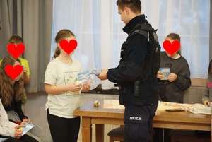 dziewczynki i chłopczyk trzymaja ulotki na temat konkursu śniezny dekalog, które im wręcza umundurowany policjant