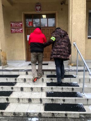 nieumundurowany policjant prowadzi zatrzymanego mężczyznę do budynku prokuratury