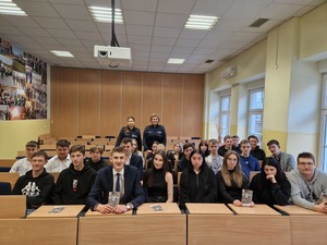 Policjantki na tle klasy. Uczniowie siedzą w ławkach szkolnych. Policjantki stoją za nimi.