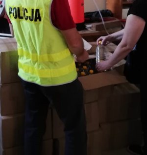 policjant w kamizelce z napisem POLICJA podczas przekazywania pracownikowi sanepidu 334 butelek spirytusu zapakowanego w kartonowych pudłach