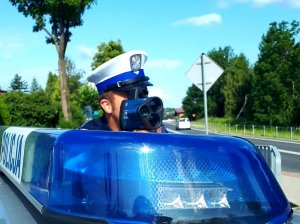 policjant z laserowym miernikiem prędkości, obok niebieska lampa na dachu