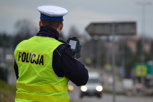 Policjant ruchu drogowego, stojący przy krawędzi jezdni, podczas pomiarów prędkości pojazdów