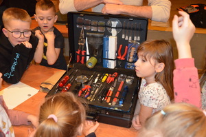 Dzieci zadają pytania policjantowi. Na stole leży walizka z narzędziami technika kryminalistyki.