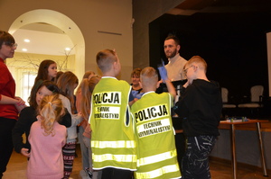 Dzieci rozmawiają z technikiem kryminalistyki. Dwoje dzieci ma ubrane kamizelki technika kryminalistyki