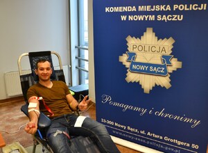 meżczyzna oddaje krew, obok baner sądeckiej Policji