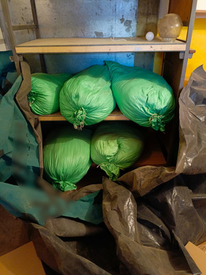 zielone worki z zawartością krajanki tytoniowej ułożone na półkach regału
