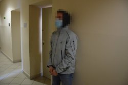 zatrzymany mężczyzna ubrany w szarą sportową kurtkę stojący przodem do zdjęcia