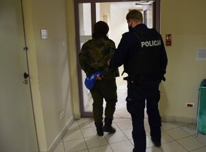 policjant prowadzący jedna z zatrzymanych osób ubraną w strój moro