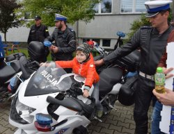 dziecko siedzące na motocyklu policyjnym obok stoi policjant z drogówki