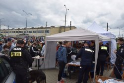stoisko profilaktyczne krakowskich policjantów obok przewodnik z psem służbowym, w tle ludzie, zabytkowe tramwaje oraz budynek zajezdni