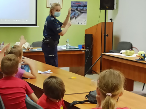 policjantka pokazuje dzieciom plakat promujący konkurs plastyczno filmowy
