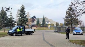 dwaj policjanci kontrolują pojazd, obok radiowóz i funkcjonariusz sterujący dronem
