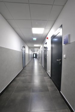 Korytarz, po prawej i lewej stronie znajdują się drzwi do pomieszczeń, obok których umieszczone są tabliczki z numerem pokoju i opisem miejsca.